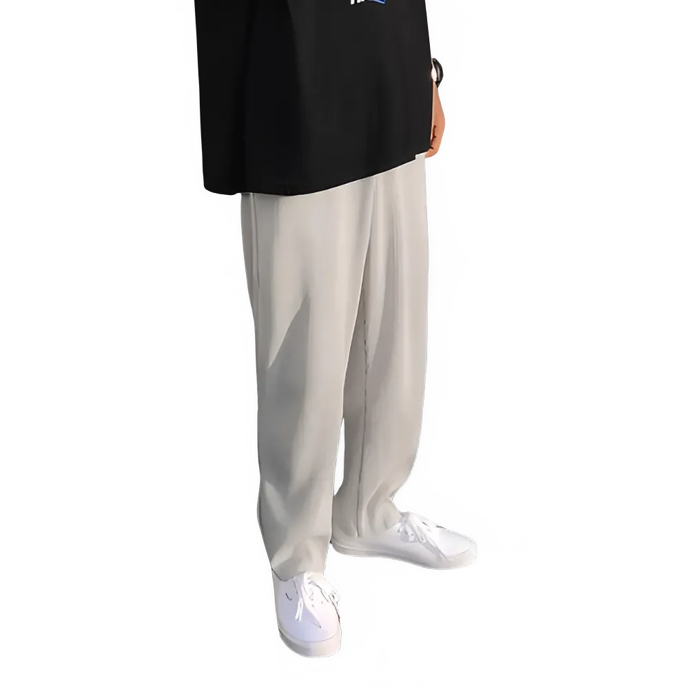 Man wearing loose beige pants with white sneakers and a black shirt on black background
