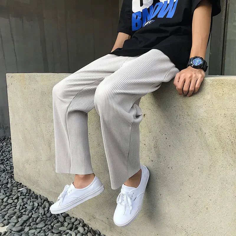 Man in ribbed beige pants, black graphic tee, white sneakers sitting on concrete wall