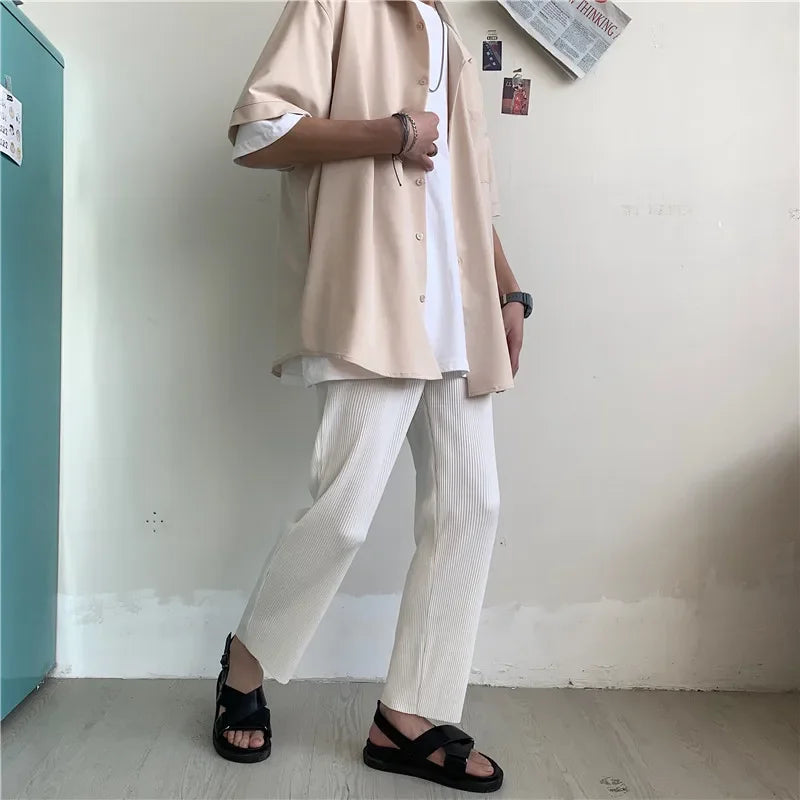 Casual outfit with beige shirt, white pants, black sandals in minimalist room