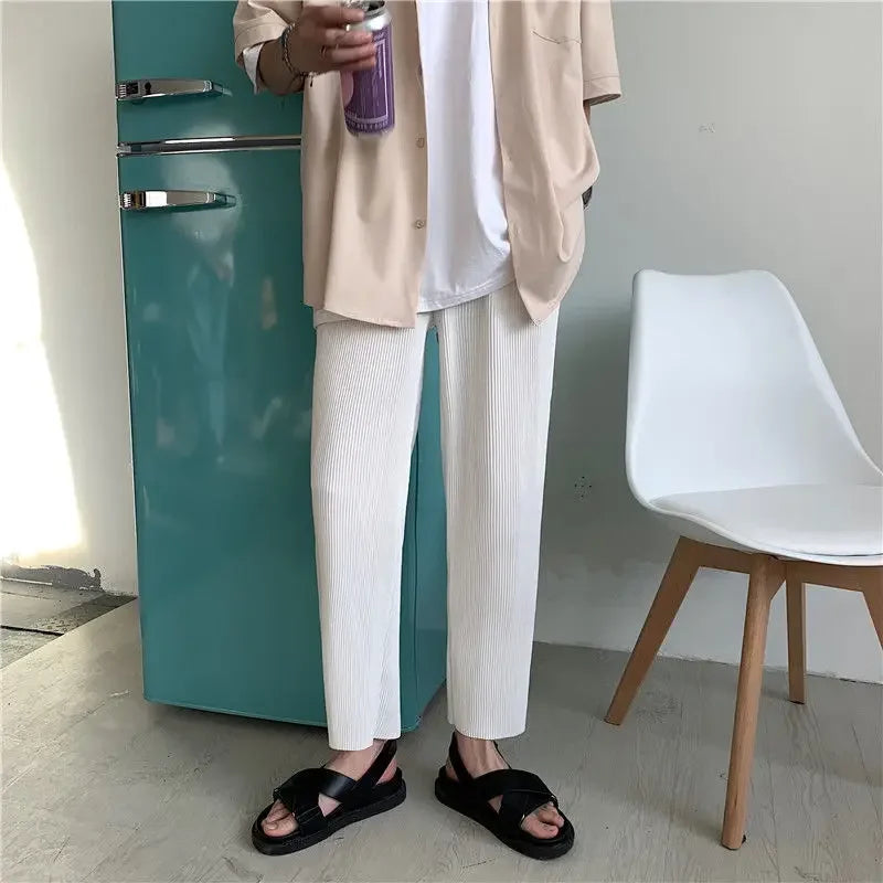 Casual outfit with beige shirt, white pants, black sandals by teal fridge and white chair