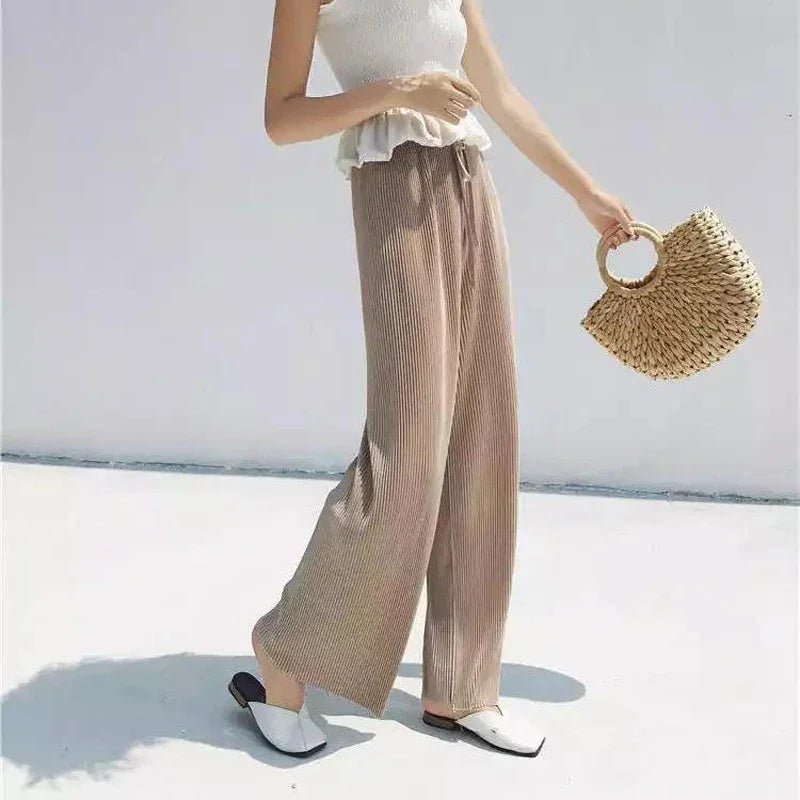Woman in beige wide-leg pants, white sleeveless top, holding woven straw handbag