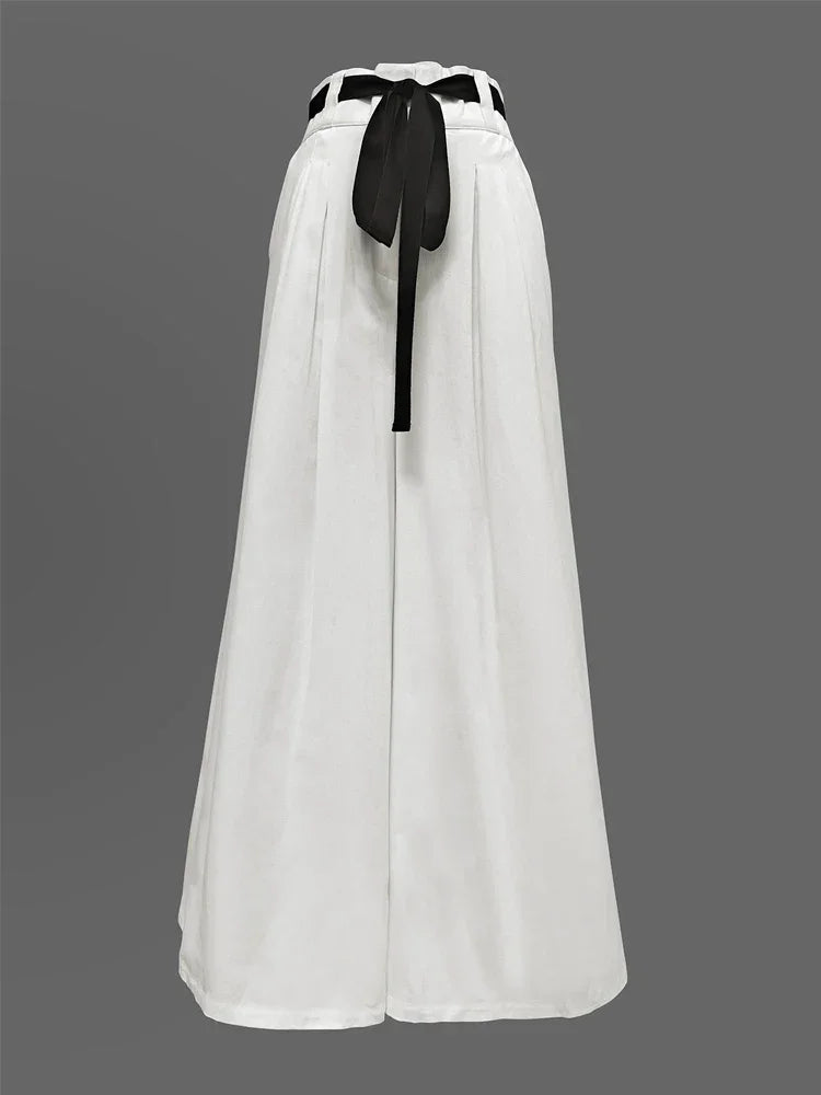 White wide-leg palazzo pants with pleats and a black ribbon belt on a gray background