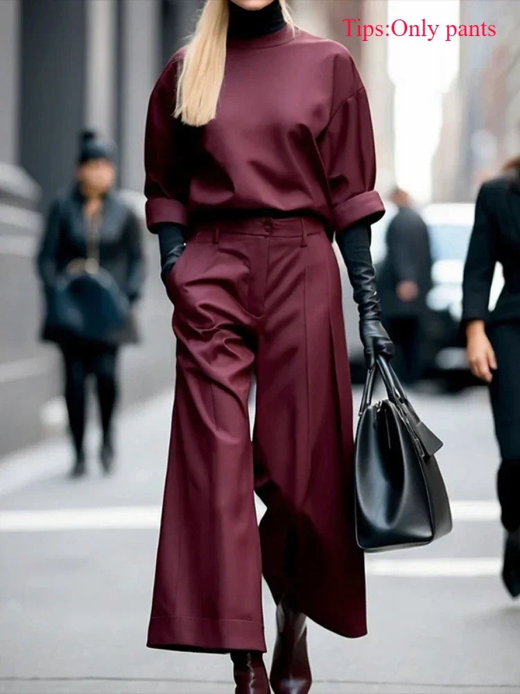 Woman wearing wide leg maroon pants, black gloves, and holding a black handbag on a city street.
