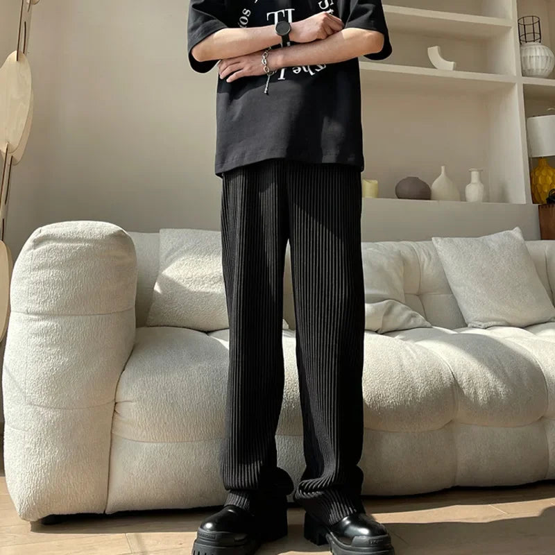 Man wearing black pleated pants and chunky shoes standing by a modern white sofa