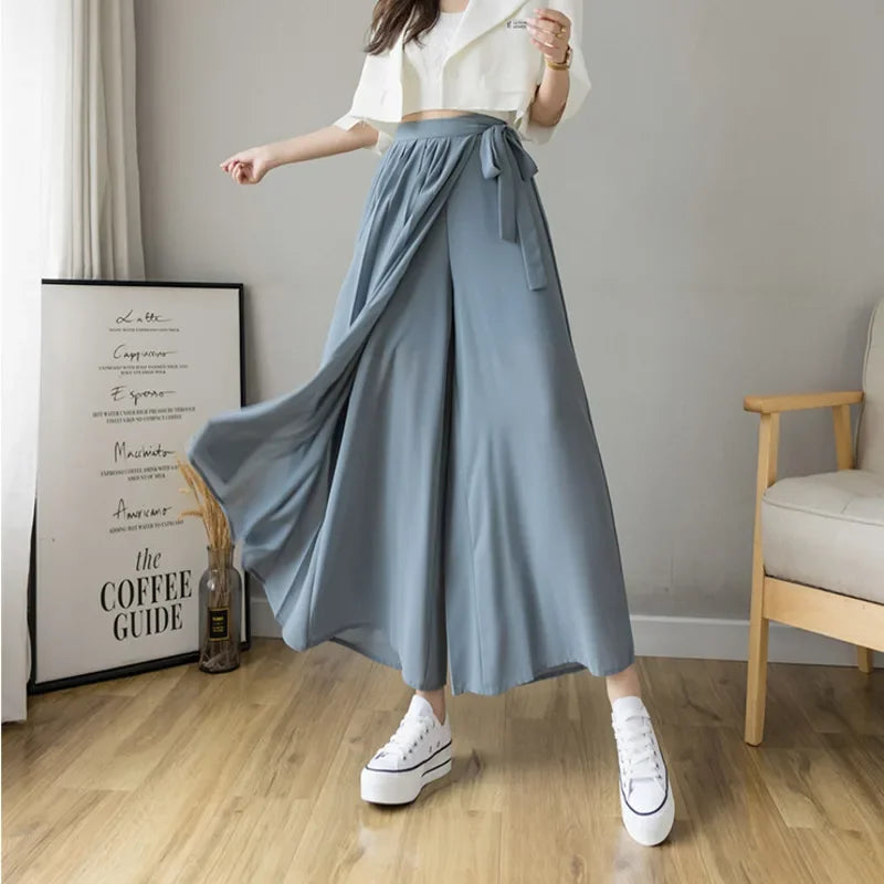 Woman wearing wide leg blue palazzo pants with tie waist and white crop top indoors