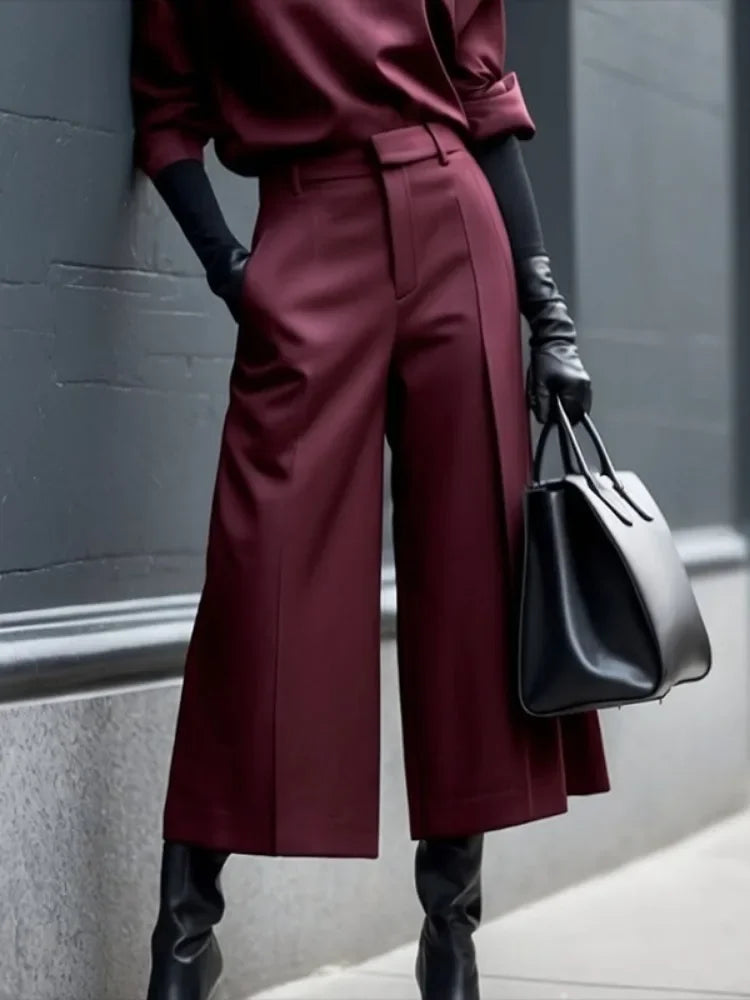 Woman in burgundy wide-leg pants and top with black gloves, black bag, and boots, city street