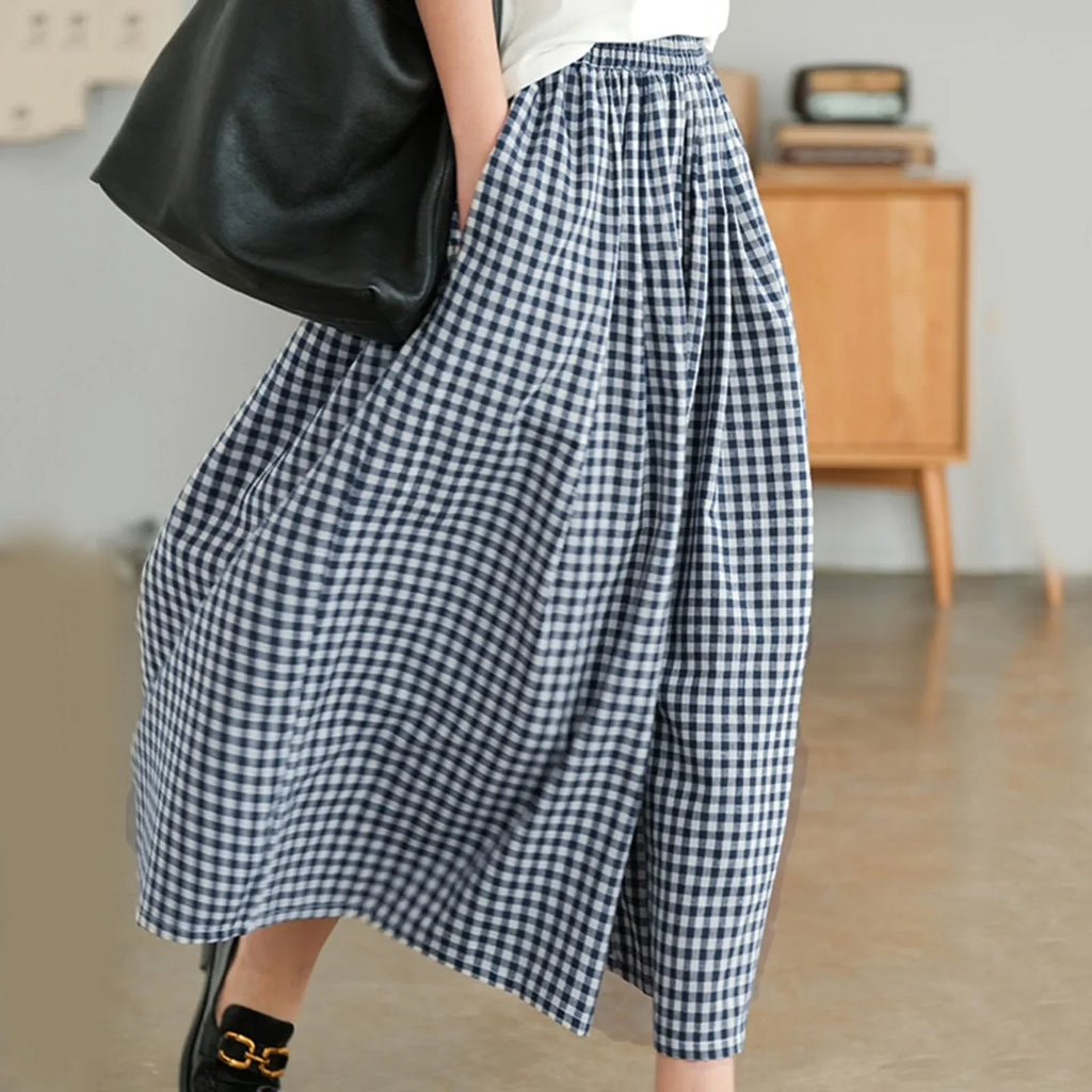 Woman wearing navy gingham midi skirt and white top, holding black tote bag indoors