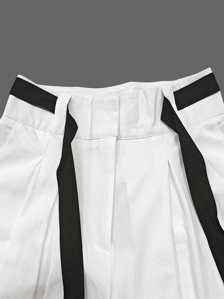 White pleated pants with black strap accents on waistband, minimalist fashion detail