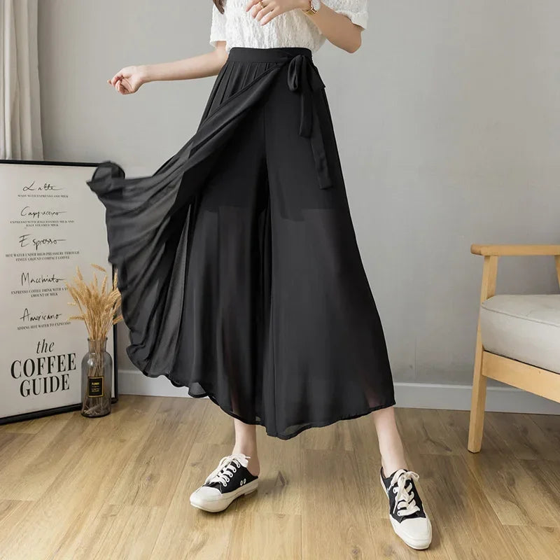 Woman wearing black chiffon wide-leg pants with white lace top and sneakers in modern room