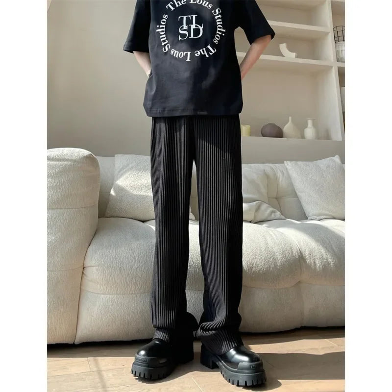 Person in black graphic t-shirt, pinstripe pants, chunky shoes, standing by cream sofa
