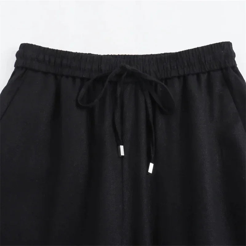 Black elastic waistband pants with drawstring and metal tips on a plain background
