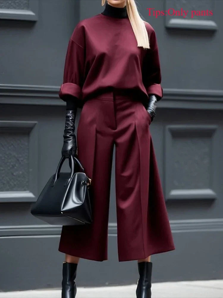 Woman wearing burgundy wide-leg pants, black gloves, heeled boots, and carrying a black handbag