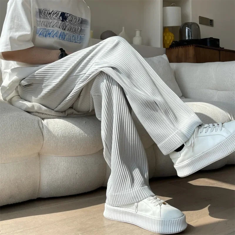Person in ribbed white lounge pants and platform sneakers sitting on a cream sofa in sunlight