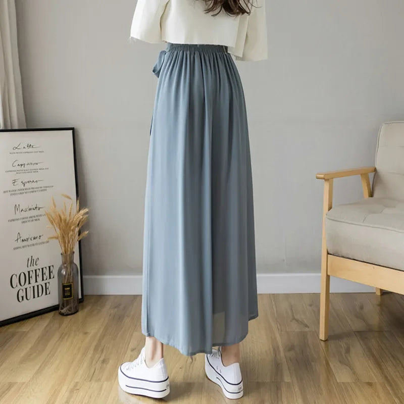 Woman in flowy blue maxi skirt and white top indoors, wearing white platform sneakers
