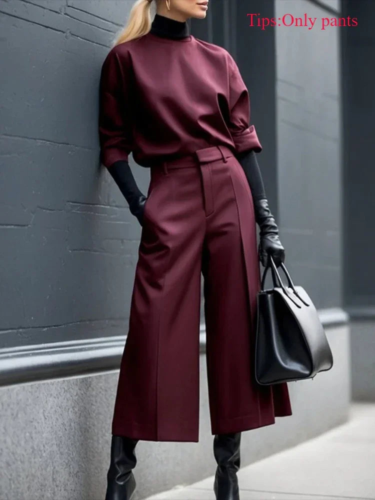 Woman wearing wide leg burgundy pants, black gloves, and holding a black handbag outdoors