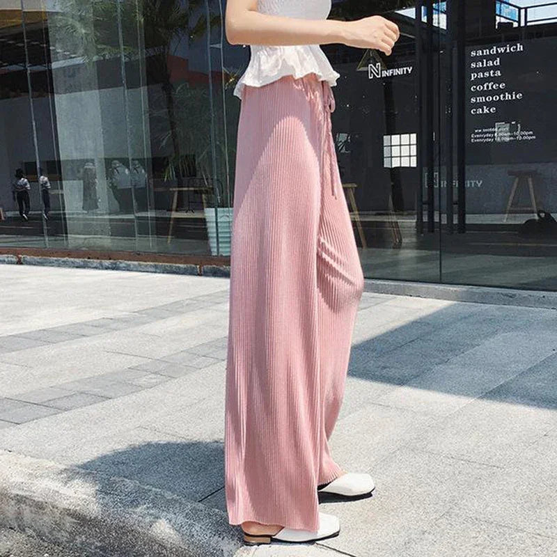 Woman wearing pink wide-leg pleated pants and white flats on urban sidewalk