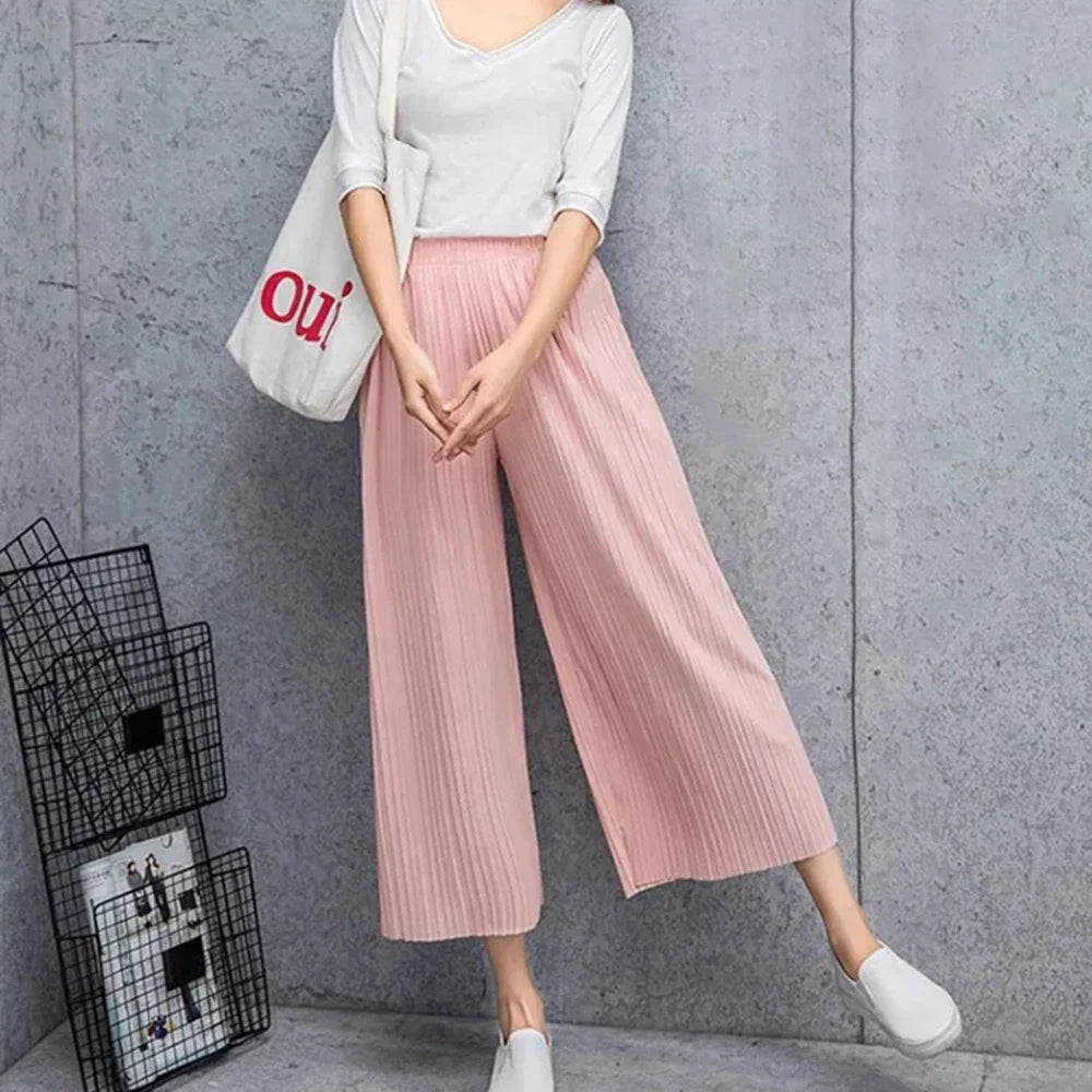 Woman in light pink pleated wide-leg pants, white top, and tote bag, casual outfit