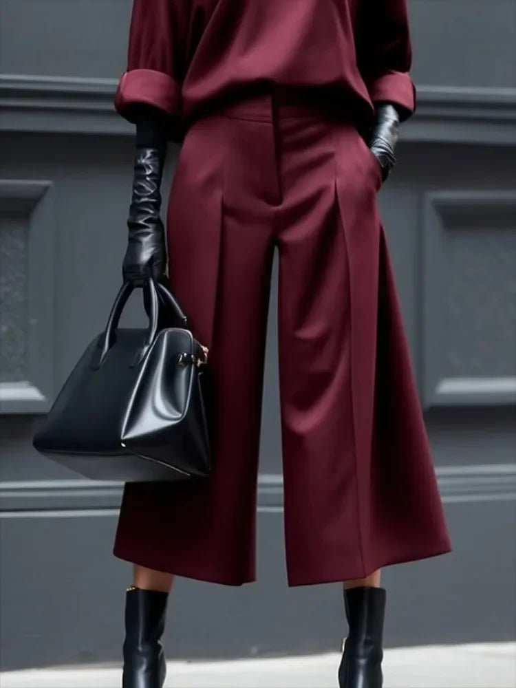 Woman wearing burgundy culottes, matching blouse, black gloves, boots, and carrying a black handbag