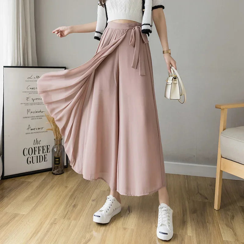 Woman wearing pink wide-leg palazzo pants with side tie, white crop top and sneakers indoors
